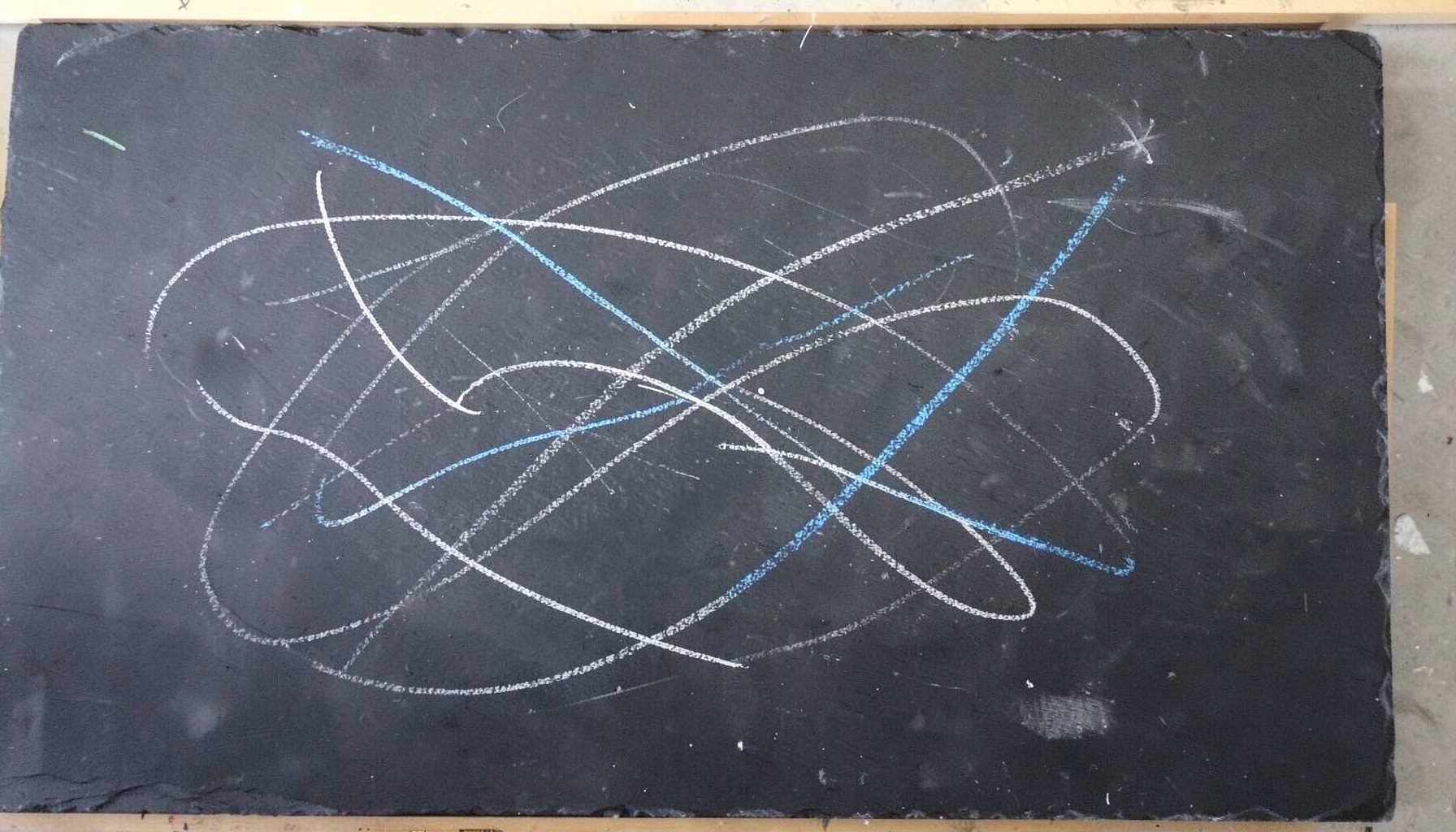 A chalk drawing on a dark slate board with satellite orbit paths and ground-track lines in white chalk, remote sensing classroom style