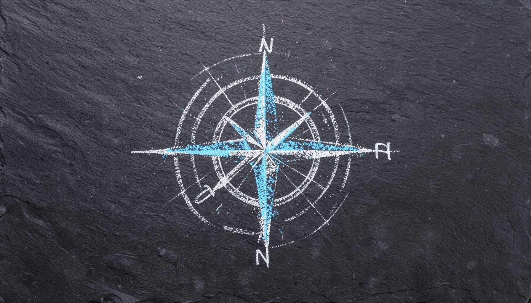 A chalk drawing on a dark slate board with a hand-drawn compass rose and bearing lines in white chalk