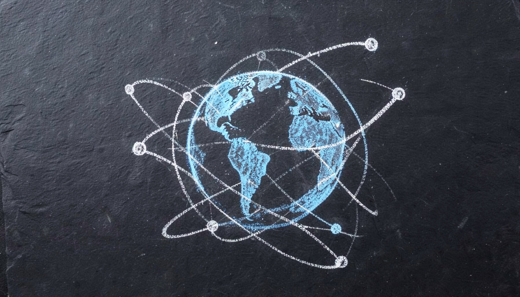 Chalk drawing on a dark slate board showing interconnected nodes and orbital paths around a stylized globe